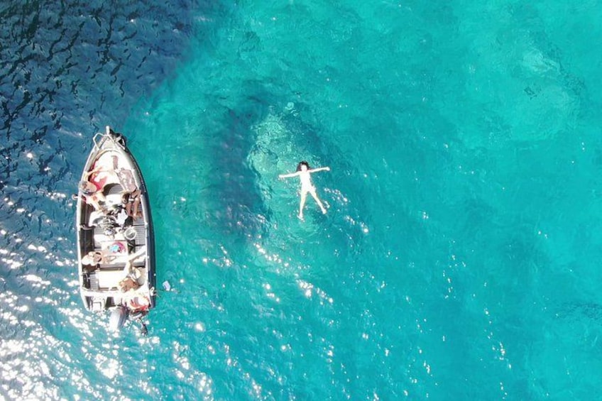 A person swimming in clear turquoise water, a boat with passengers, and a rocky shoreline. 3