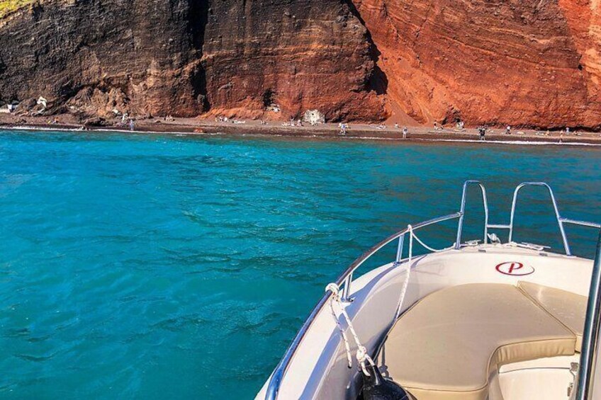 A boat with a lifebuoy and a red symbol on the bow, a clear blue sea, and a rocky cliff with people on the shore. 5