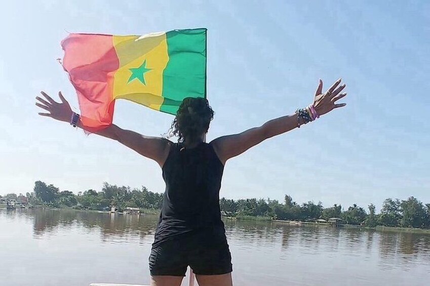 Una persona sosteniendo una bandera con una estrella y franjas, de pie junto a un cuerpo de agua tranquilo con cielo despejado. 2