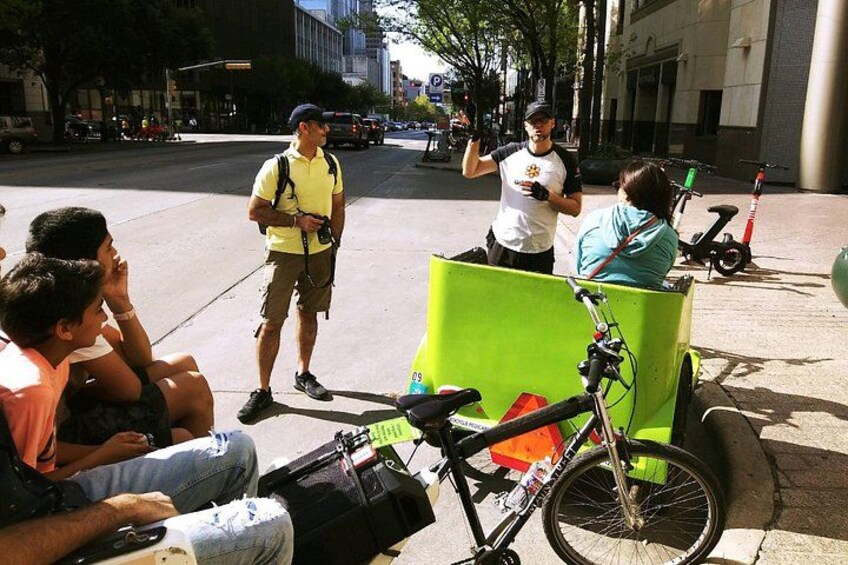 Escena callejera con un carrito verde, una bicicleta y personas sentadas en la acera. 4