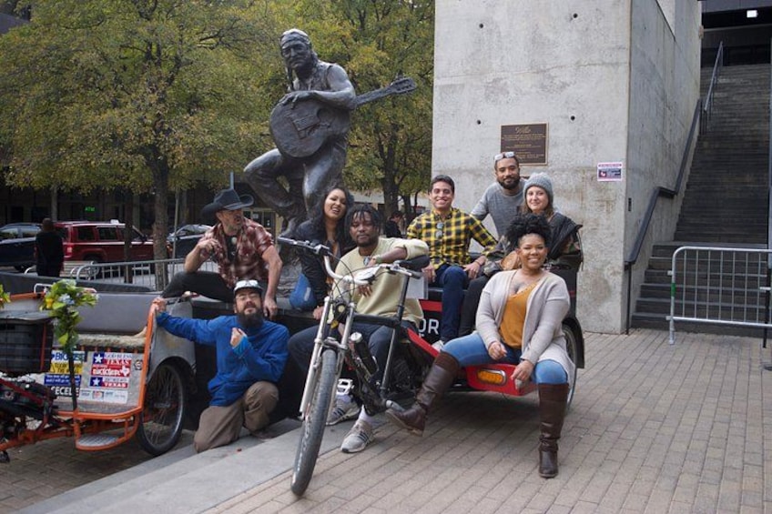 Un grupo de personas posando con una motocicleta y una estatua en un entorno urbano. 5