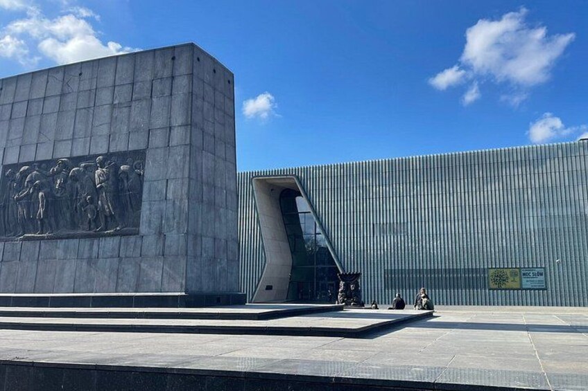 A modern building with a large relief sculpture on the left and a curved glass entrance on the right. 4