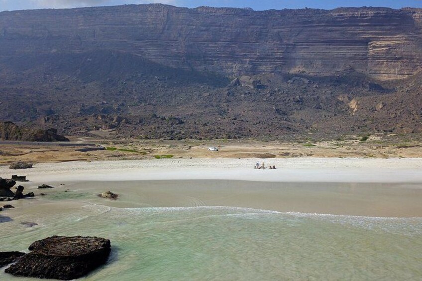 Un paisaje costero con una playa, agua cristalina y un acantilado rocoso al fondo. 1