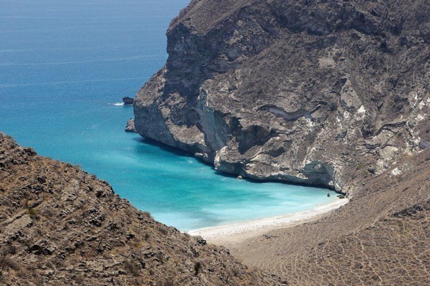 Un paisaje costero con un acantilado rocoso, mar turquesa y una playa arenosa. 4