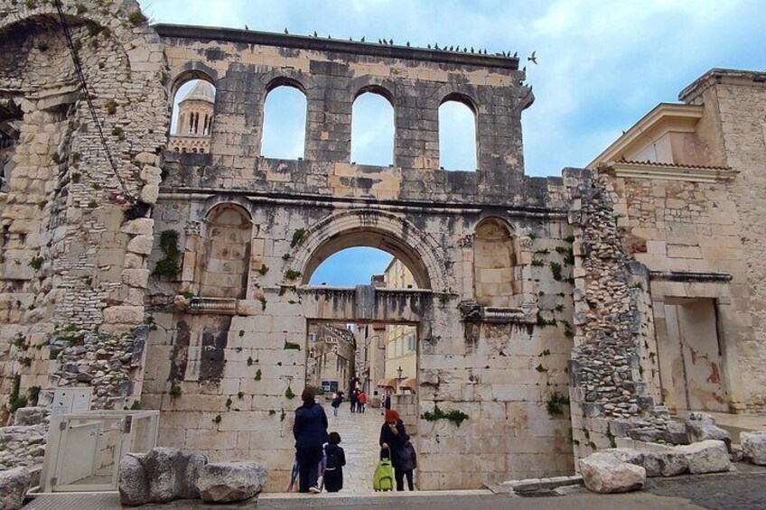 Un antiguo arco de piedra con tres aberturas arqueadas, rodeado de ruinas y vegetación. 2