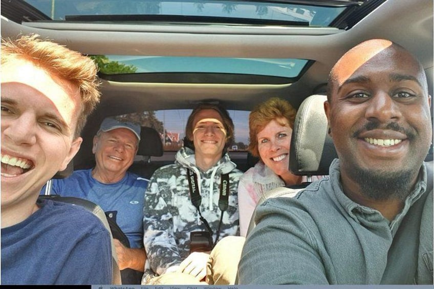 A group of people inside a car, with a sunroof and a seatbelt visible. 2