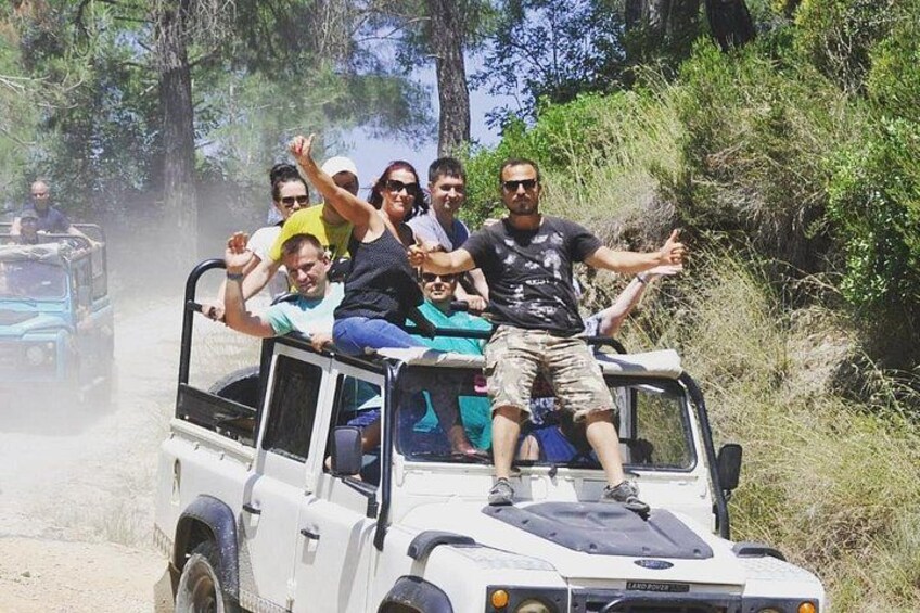 A group of people on a safari vehicle in a natural setting with trees and a dirt path. 1
