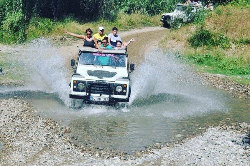 A white off-road vehicle driving through a shallow water crossing with people on board. 5