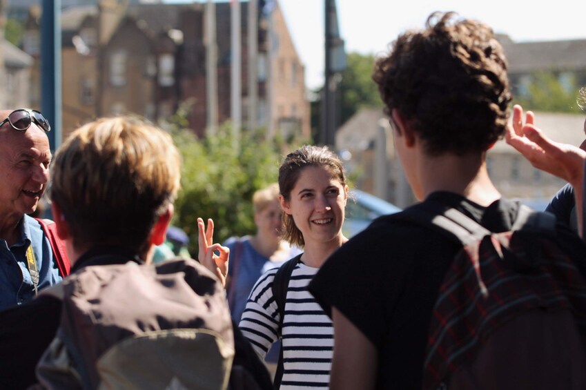 A group of people standing outdoors, some with backpacks, in an urban setting with buildings and trees in the background. 4