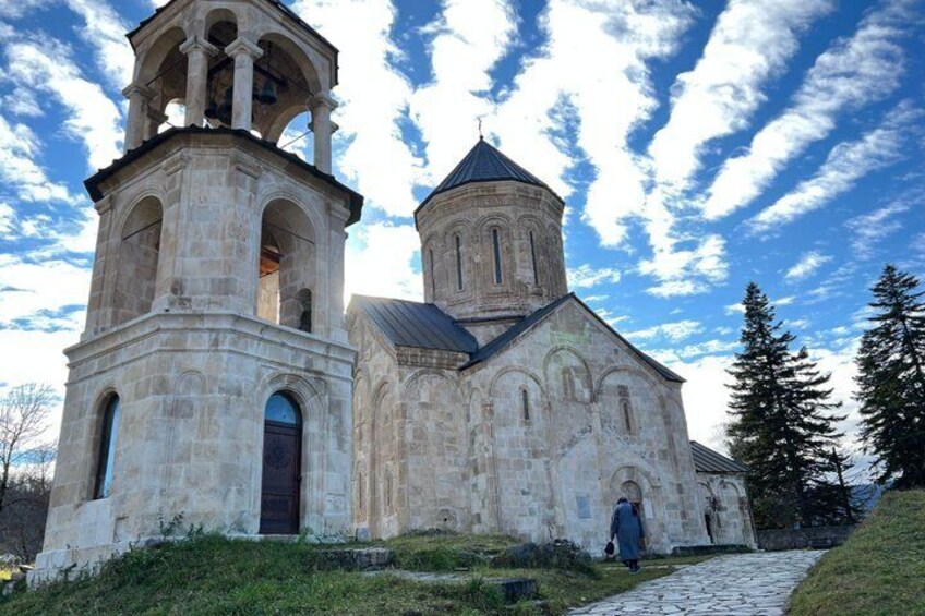 A stone church with a bell tower and a dome, surrounded by trees and a clear sky. 4