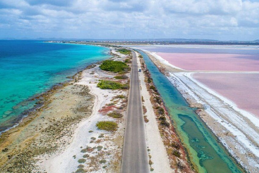 Een kustweg met een strand aan de ene kant en een roze zoutwaterlagune aan de andere kant. 1