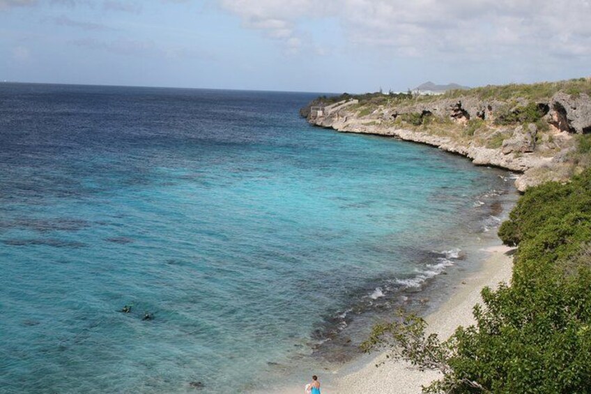 A coastal landscape with clear turquoise waters, a sandy beach, and rocky cliffs. 3