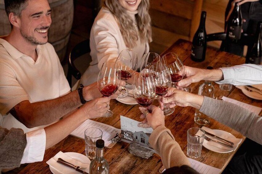 A group of people toasting with wine glasses at a wooden table. 5