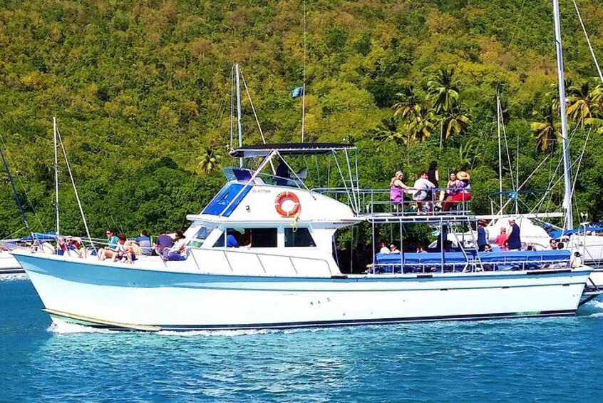 Un barco blanco con detalles azules, pasajeros en la cubierta y una isla boscosa al fondo. 2