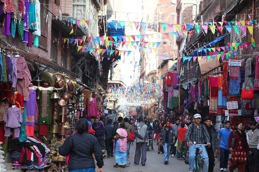 A crowded market street with stalls selling textiles and other goods. 1