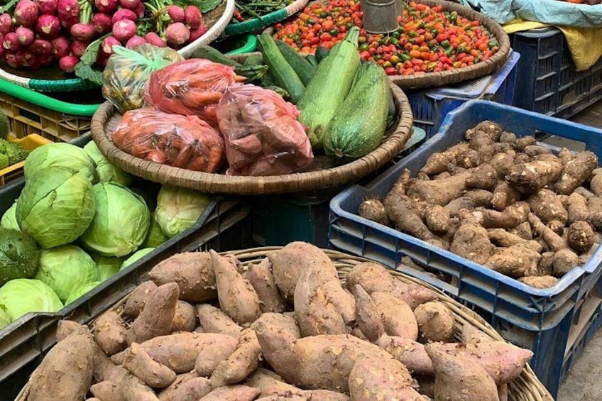 A variety of fresh produce including cabbages, sweet potatoes, and tomatoes displayed in baskets and crates at a market. 5
