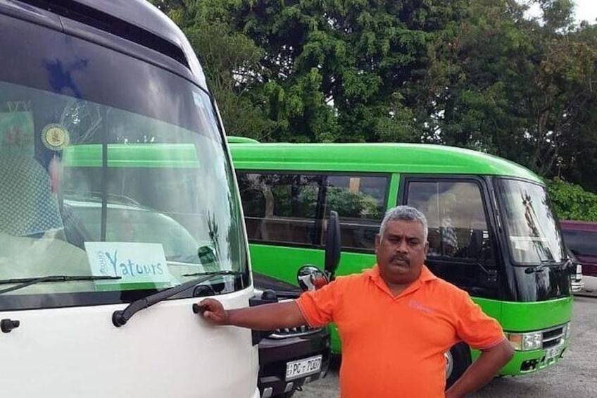A man in an orange shirt standing next to a white and green bus with a sign on the windshield. 1
