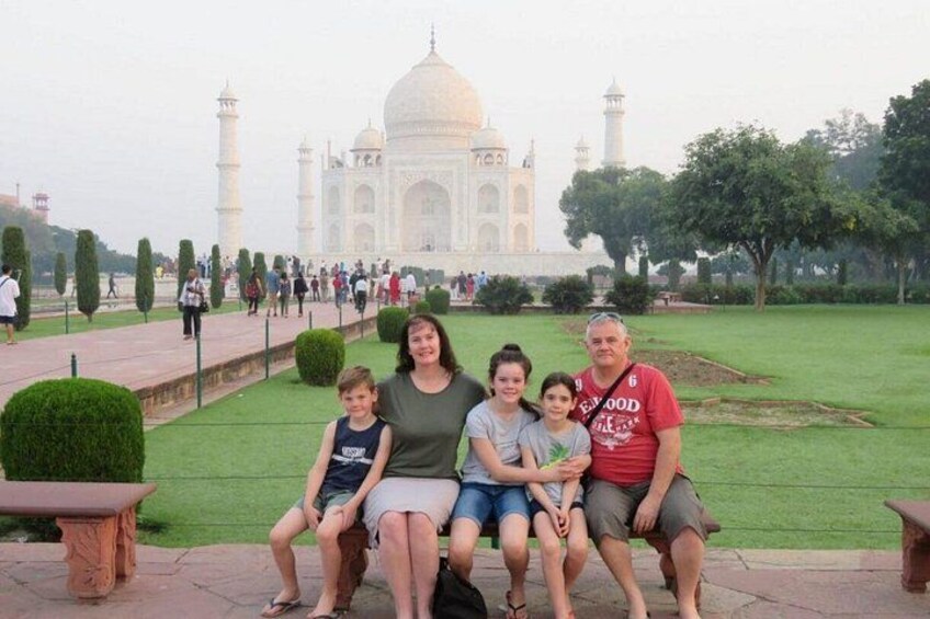 A family sitting in front of the Taj Mahal with a well-maintained garden and a clear sky. 2