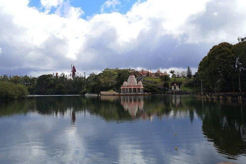 A calm lake with a gazebo, trees, and a distant building. 3