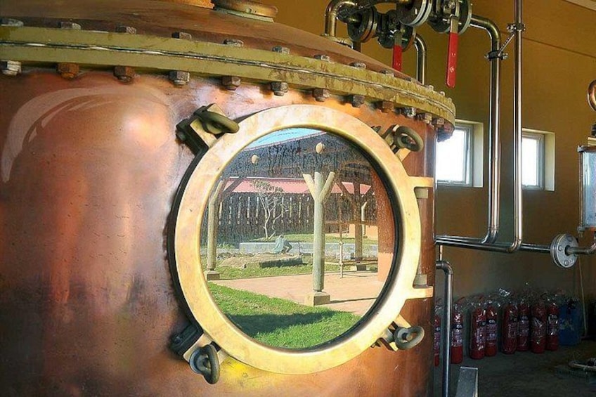 A large copper still with a window, pipes, and fire extinguishers in the background. 4
