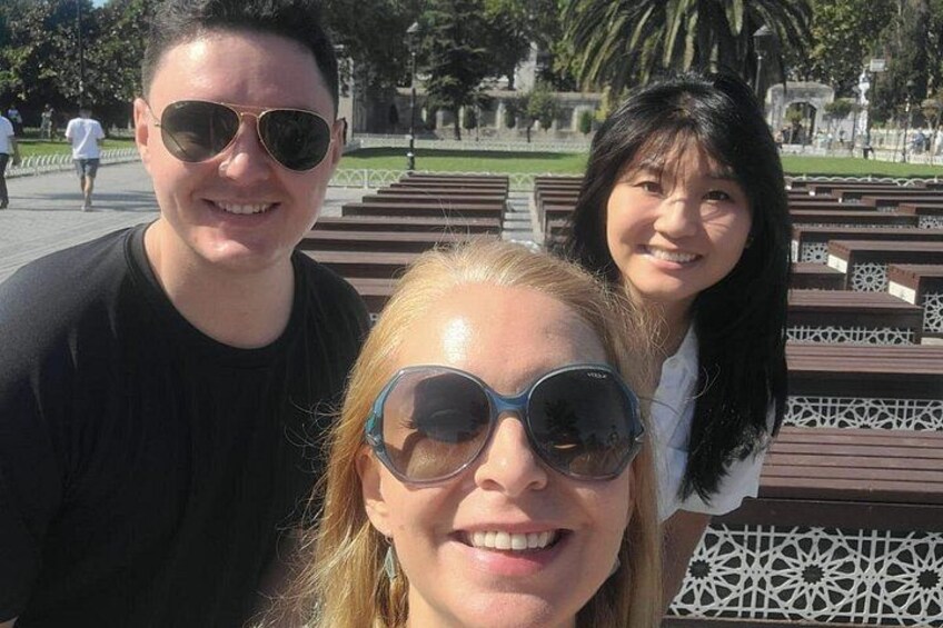 Three people in a park with benches and a patterned fence in the background. 4