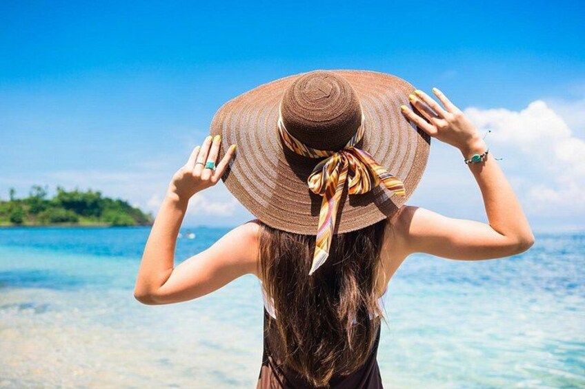 Una persona con sombrero de ala ancha y bufanda, parada frente a un mar azul cristalino con una isla a lo lejos. 1