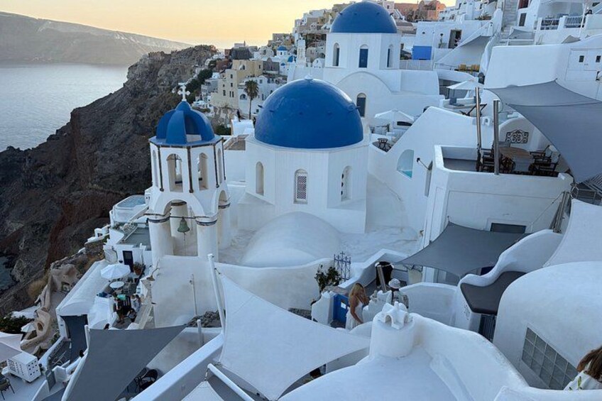 A coastal town with white buildings and blue domes, a cliff, and the sea. 3
