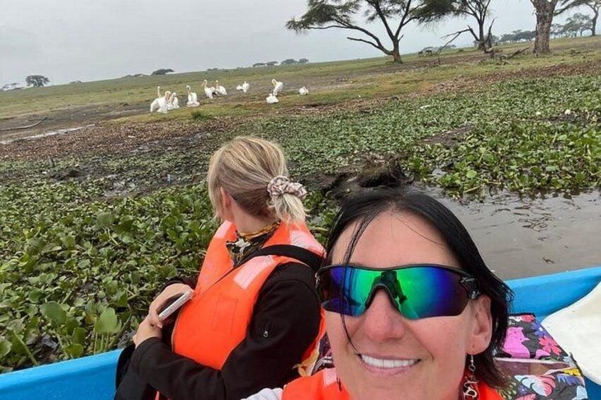 Two people in a boat on a water body with vegetation and birds in the background. 1
