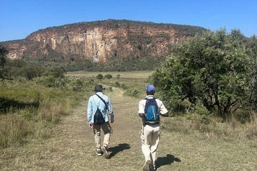 Two people walking on a dirt path with a large cliff in the background. 3