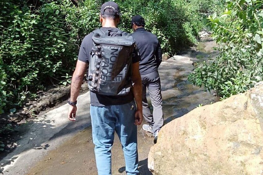 Two people walking along a narrow path surrounded by greenery. 3