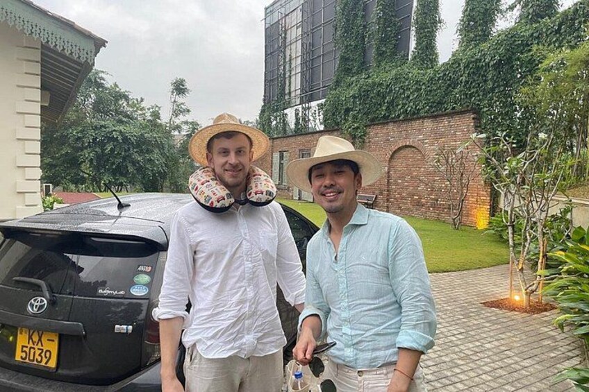 Two people standing next to a car with a brick wall and greenery in the background. 2