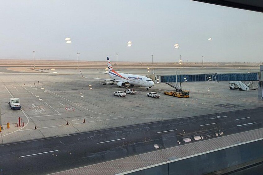 An airport tarmac with a large airplane parked, ground service vehicles, and airport infrastructure. 4