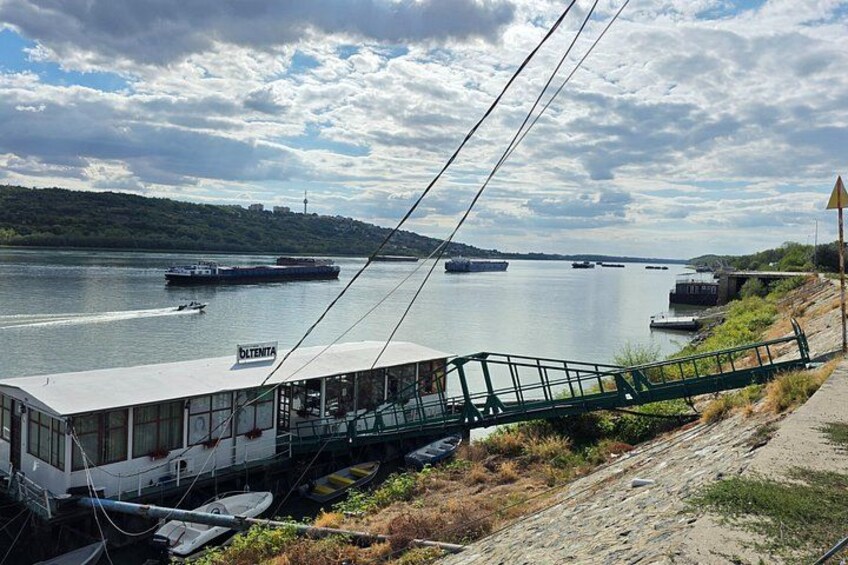 A river with boats, a train on tracks, and a bridge in the background. 1