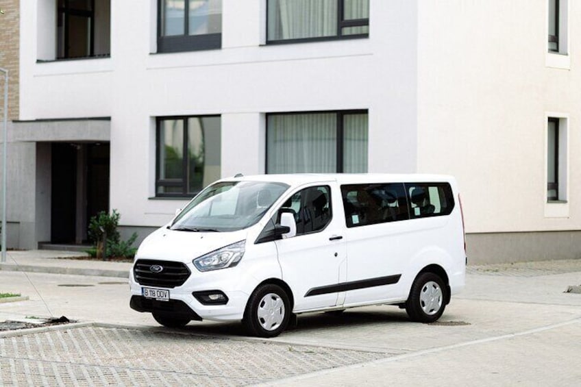 A white van parked in front of a modern building with large windows and a paved sidewalk. 2