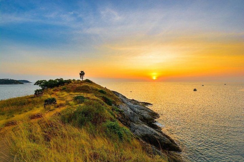 A sunset over a coastal landscape with a grassy hill, a lone tree, and calm water. 5