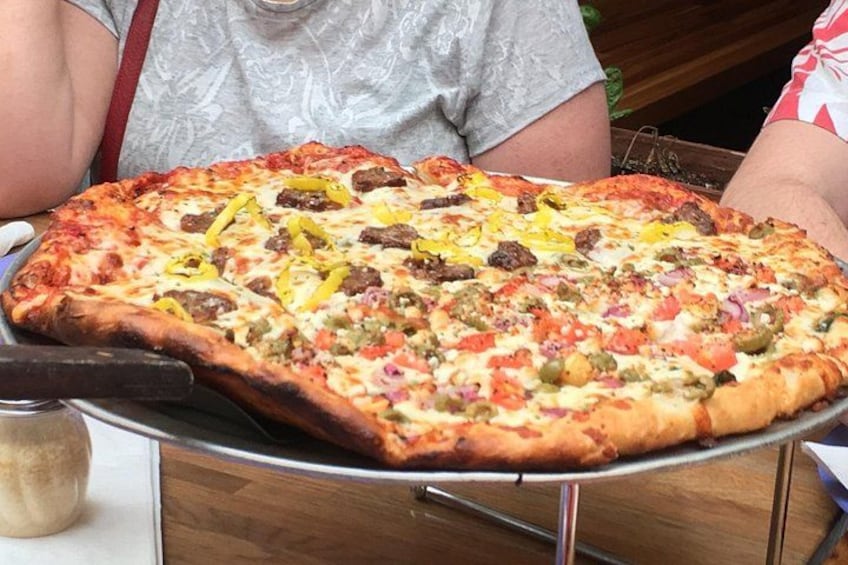 En stor pizza med olika sorters pålägg, serverad på en metallbricka. 3