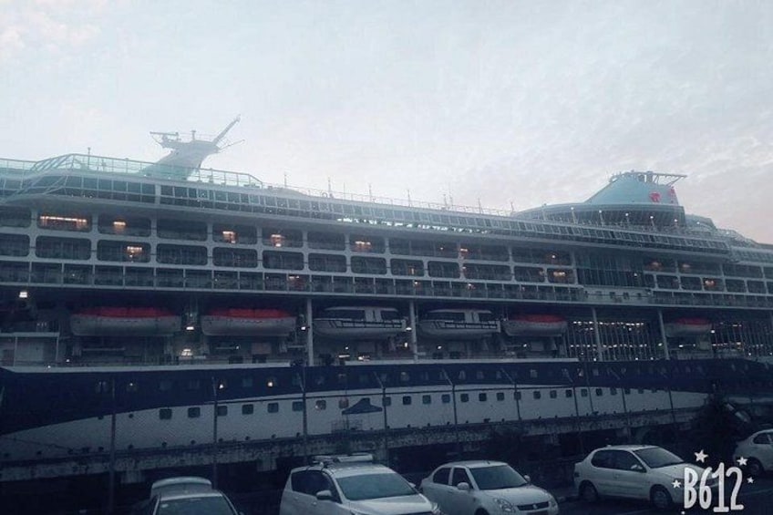 Ein großes Kreuzfahrtschiff liegt im Hafen, vor dem mehrere Autos geparkt sind. 1
