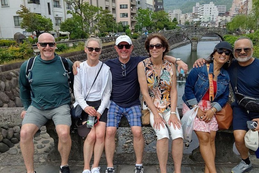 A group of people sitting on a stone wall with a river and buildings in the background. 3