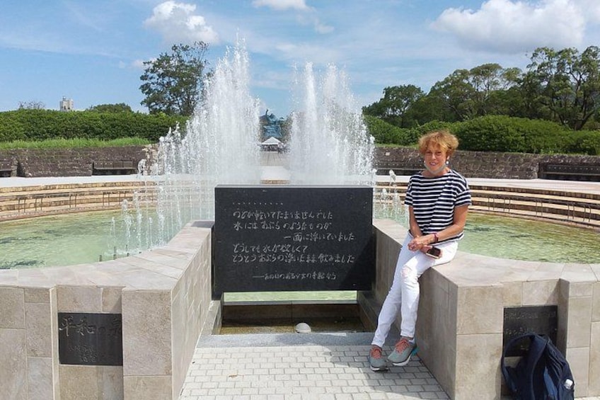 A person sitting by a fountain with a sign in front of them. 5