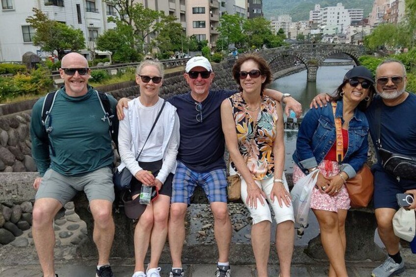 A group of people sitting on a stone wall by a river with buildings in the background. 3