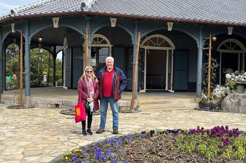A covered pavilion with a tiled roof, stone steps, and a flower bed with purple and yellow flowers. 2