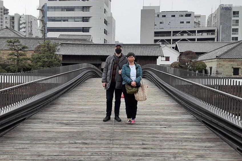 A wooden pedestrian bridge with metal railings, surrounded by modern buildings and traditional architecture. 3