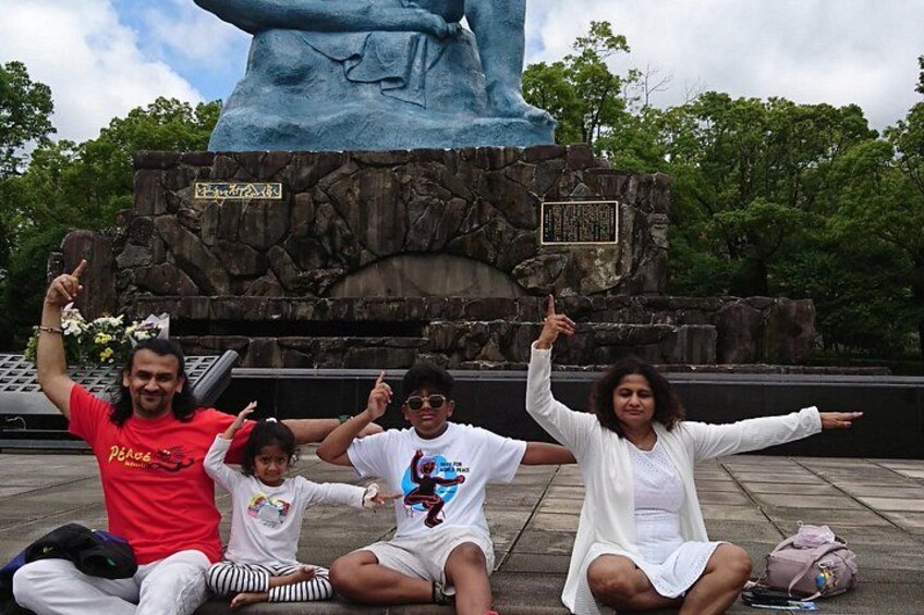 A family posing in front of a large blue statue with a stone base, surrounded by trees. 4