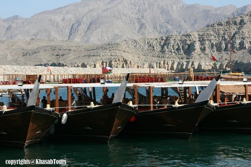 A row of traditional wooden boats docked at a pier with mountains in the background. 4