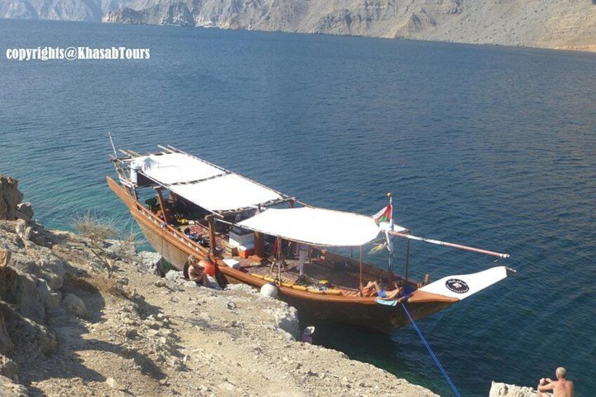 A boat docked at a rocky shore with a clear view of the water and distant mountains. 1