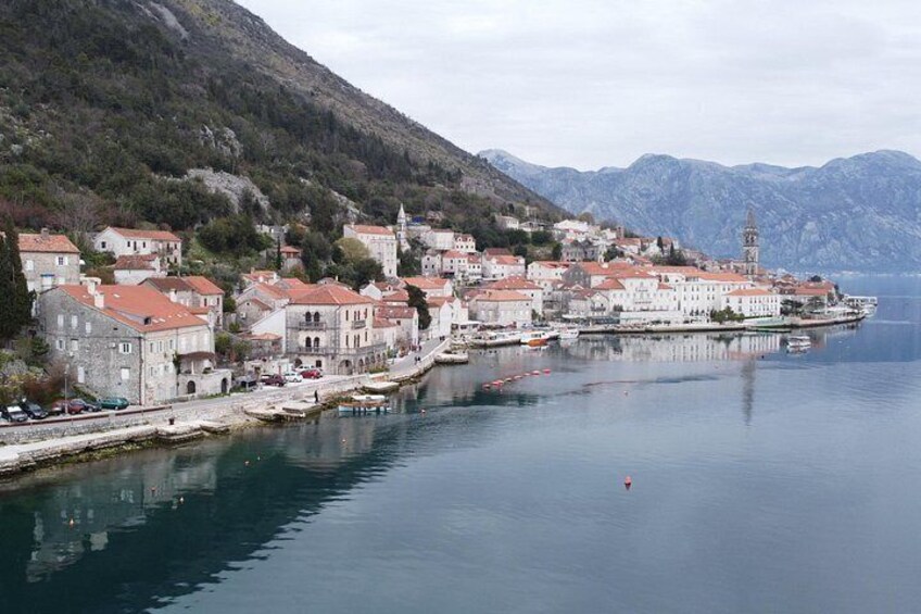 A coastal town with buildings along the waterfront, a clear sky, and mountains in the background. 3