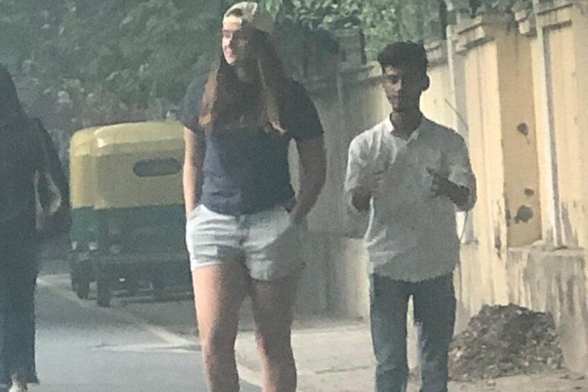 A street scene with a yellow auto-rickshaw, a woman in a black top and white shorts, and a man in a white shirt and jeans. 2