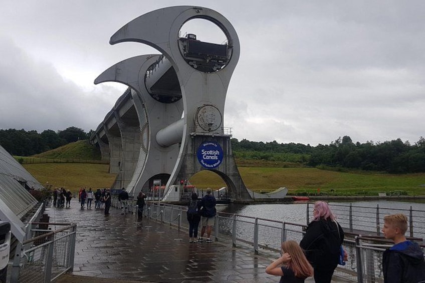 Une structure architecturale moderne au design circulaire, un panneau indiquant un lieu, et une étendue d’eau en arrière-plan. 3