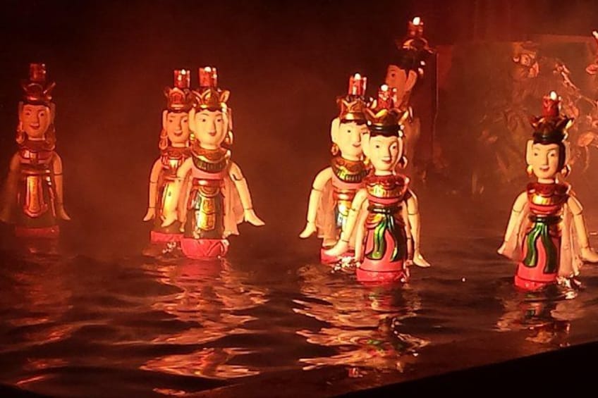 A group of traditional figures in costumes, possibly for a cultural performance, standing in water with reflections. 2
