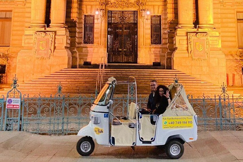 Een witte tuk-tuk geparkeerd voor een statig gebouw met een trap die naar een grote deur leidt. 3